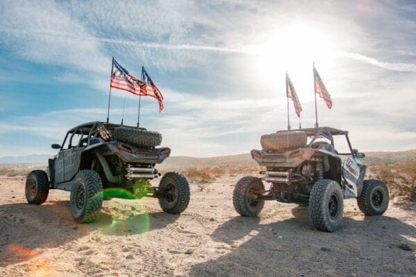 Two atv 's parked in the desert with american flags on them.