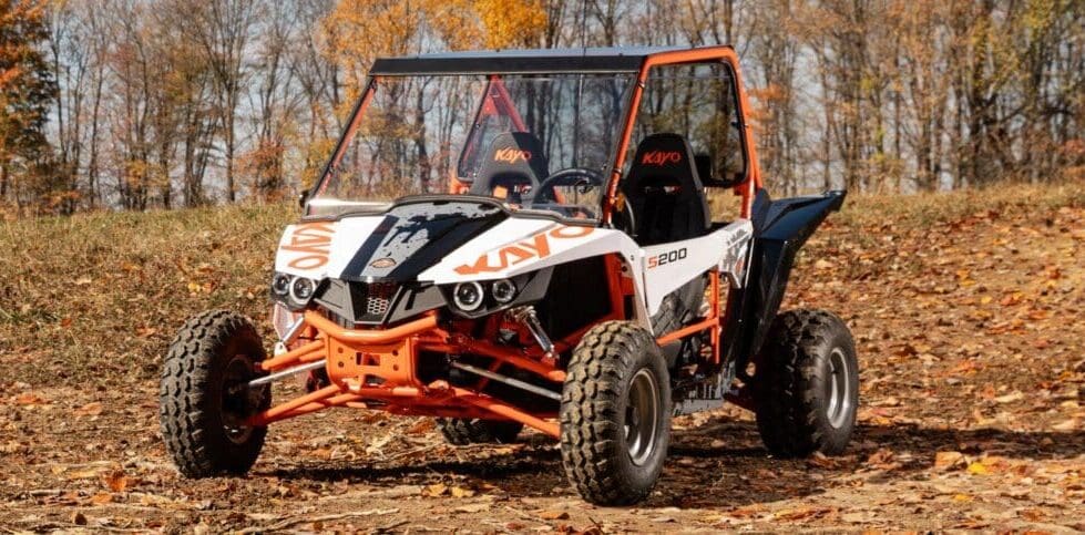 A white and orange buggy is driving through the woods.